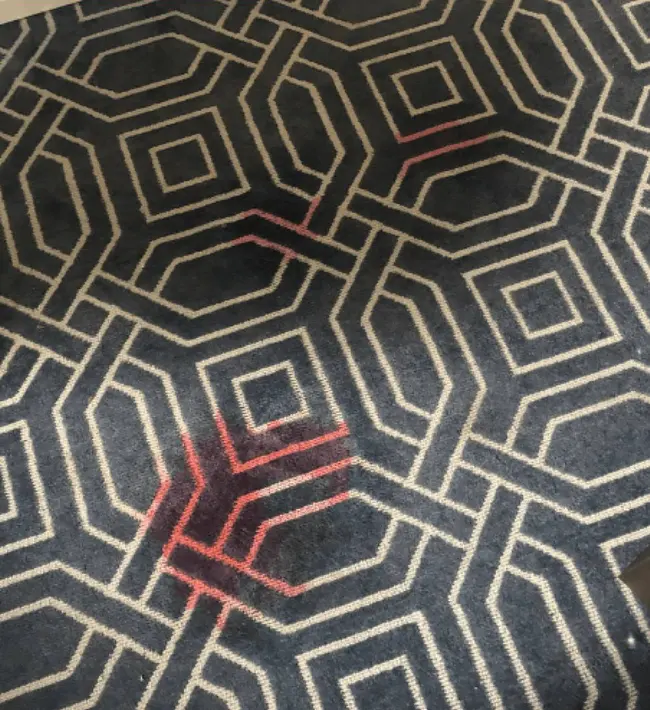 Before carpet treatment: red wine staining on the patterned hotel room carpet